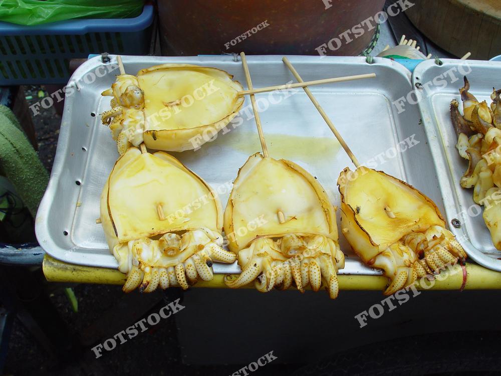 Фотография посвящена уличной еде, приготовленной из морепродуктов. Свежевыловленные кальмары приготовлены на гриле и размещены на металлическом подносе.